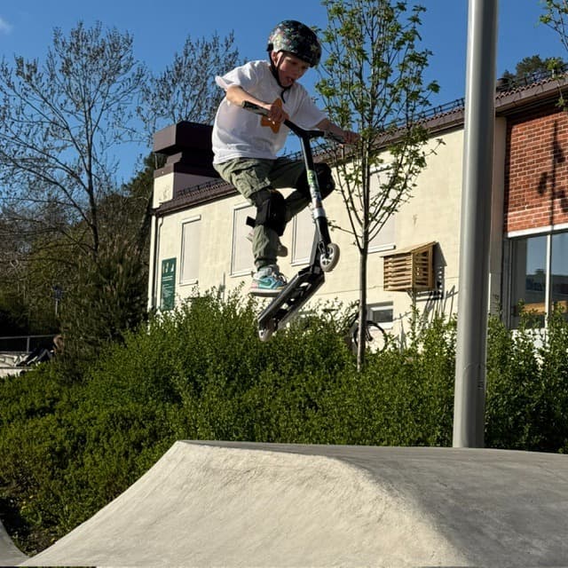 Ung scooterkjører i luften på skatepark